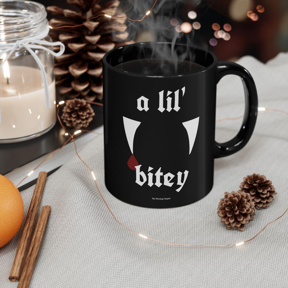 Black gothic vampire mug featuring the phrase a lil’ bitey with white fang artwork and a red blood drop design printed on both sides.